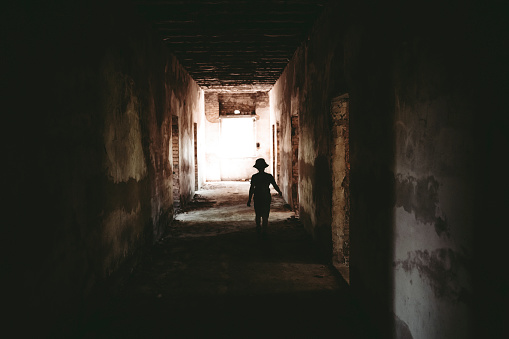 The dark silhouette of a child in a hat against the background of a bright exit from the tunnel.
