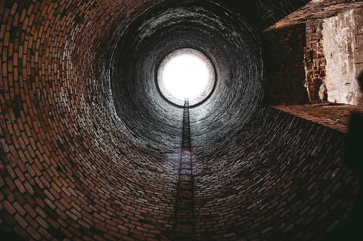 Interior view of an old industrial smoke chimney with a ladder and a circular bright outlet.