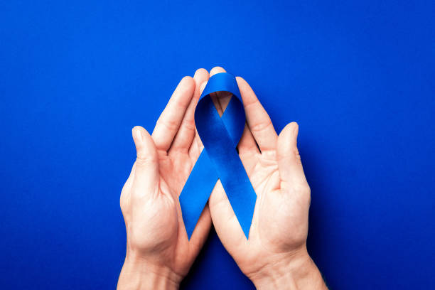 青いリボン癌。11月の男性の健康の意識前立腺癌。深い青色の背景に分離された手の青いリボン。腫瘍学のシンボル 影響を受けた人 コピースペース - 十一月 ストックフォトと画像