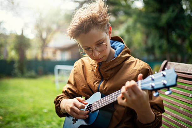 Portrait of Asian boy playing classic ukulele with looking camera while standing outdoor in the summer garden.