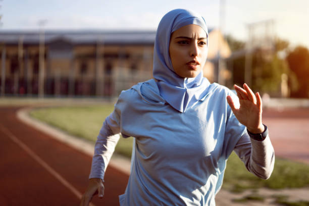 мусульманка в скромной спортивной одежде и хиджабе бежит по спортивной дорожке - real people healthy lifestyle one person effort стоковые фото и изображения