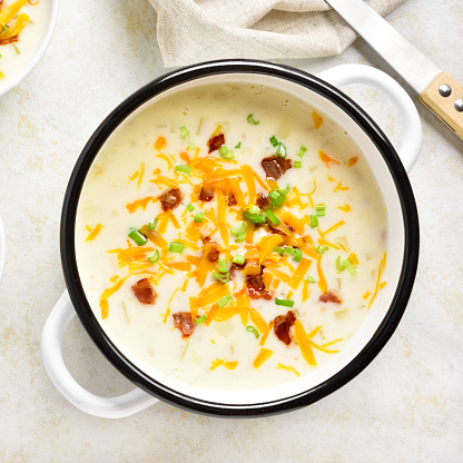Close up view of creamy potato soup with bacon and cheddar cheese in bowl on light stone background. Top view, flat lay