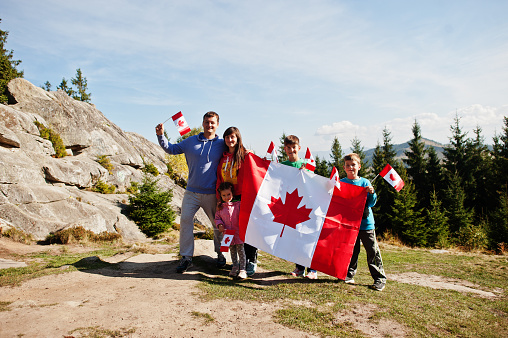 Happy Canada Day. Family with large Canadian flag celebration in mountains.