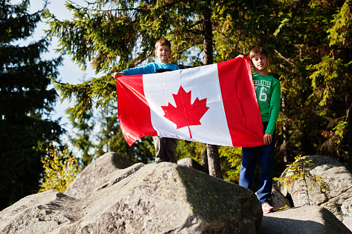 Happy Canada Day. Two brothers with large Canadian flag celebration in mountains.