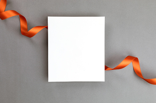 White blank empty card on gray background wrapped with a orange colored ribbon.