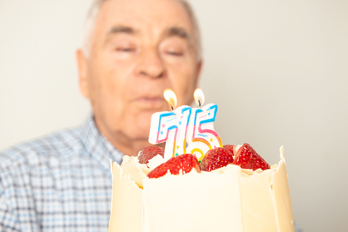 Senior man making a wish and blowing candles on his lovely birthday cake.