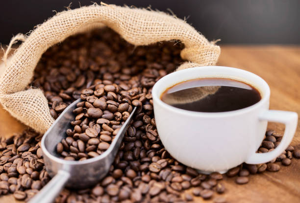 aufnahme von kaffeebohnen und einer tasse schwarzem kaffee auf einem holztisch - kaffee stock-fotos und bilder