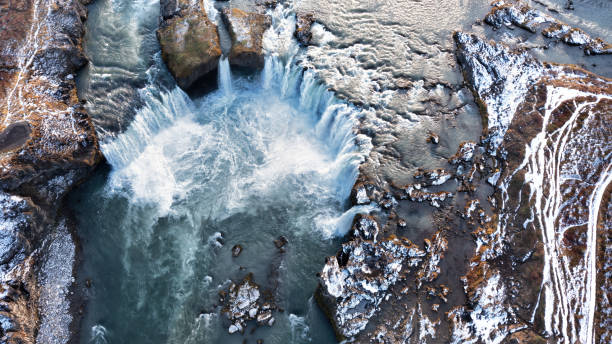 tiro drone da cachoeira godafoss, islândia, tirada diretamente de cima. vista aérea da poderosa cascata, rio e neve cobertas de rochas. - mist rock winter autumn - fotografias e filmes do acervo