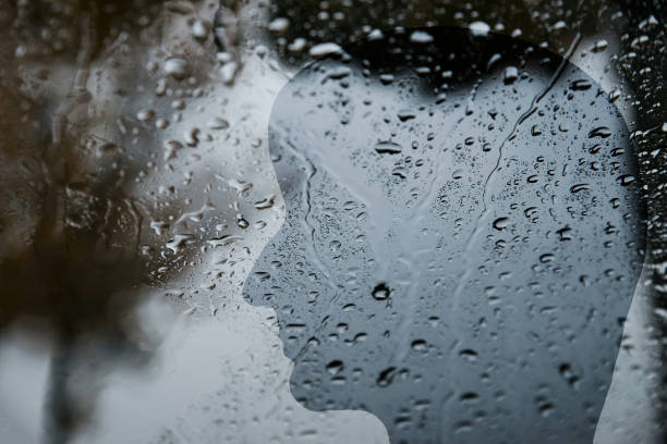 istock Silhouette of a human face behind a window with raindrops, dark, depression, loneliness, negative emotions 1349243372