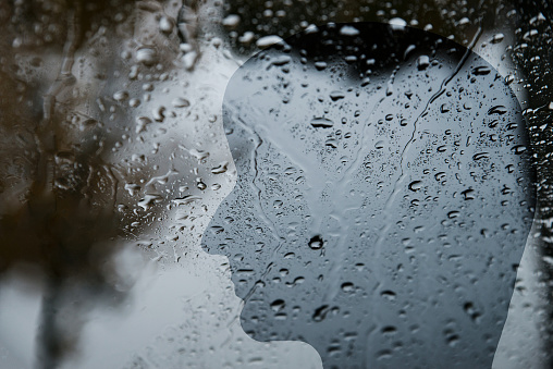 Silhouette of a human face behind a window with raindrops, dark, depression, loneliness, negative emotions