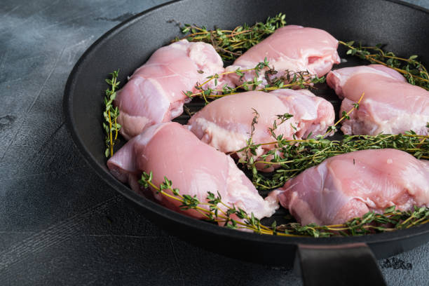 muslos de pollo crudos sobre hierro fundido sobre fondo gris - chicken thighs fotografías e imágenes de stock