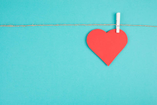 A heart hanging on a clothing line, blue colored background, empty copy space, symbol of love, valintine greeting card stock photo