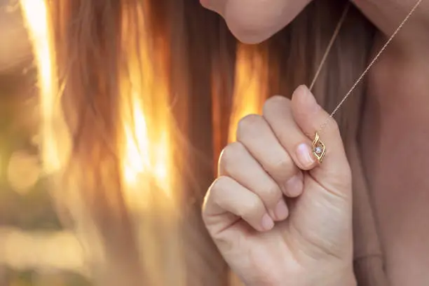 Woman with a Beautiful Pendant on her Neck in Mild Sunlight. Golden Chain with Little Precious Stone. Luxury Jewelry.