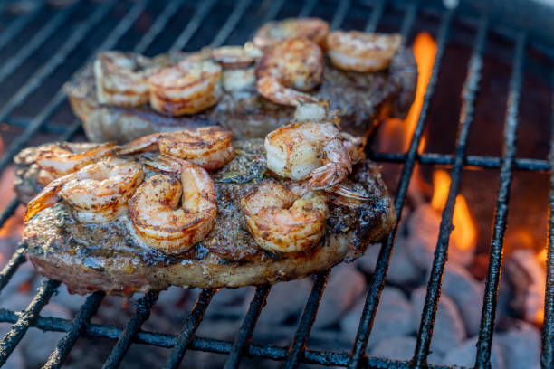 délicieux steak de côte de bœuf garni de beurre et de crevettes sur un gril avec du feu sur un gril au charbon de bois - surf and turf prepared shrimp seafood steak photos et images de collection