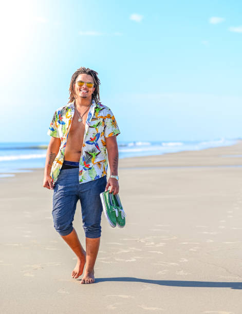 istock Handsome happy mixed race young guy walking barefoot on an idyllic beach in sunglasses 1349256740