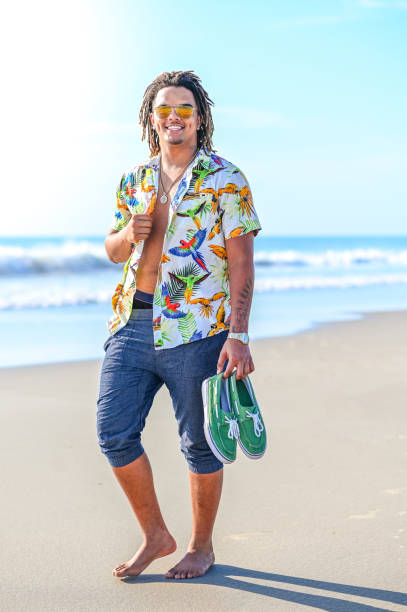 istock Handsome happy mixed race young guy walking barefoot on an idyllic beach in sunglasses 1349256816