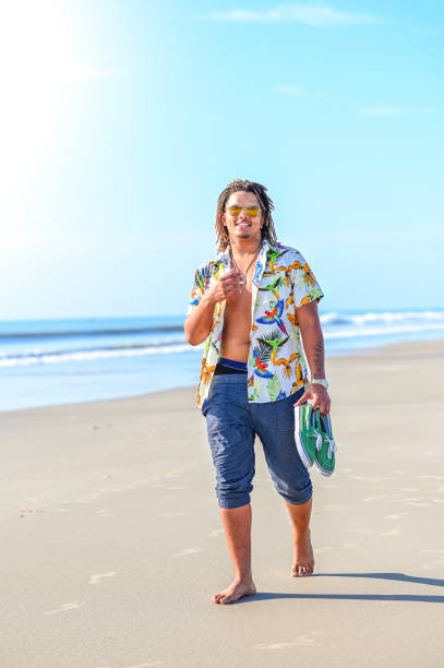 istock Handsome happy mixed race young guy walking barefoot on an idyllic beach in sunglasses 1349256817