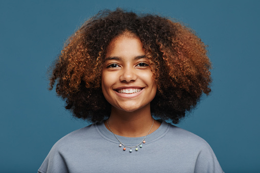 Minimal portrait of young African-American woman with natural curly hair looking at camera in studio against blue background