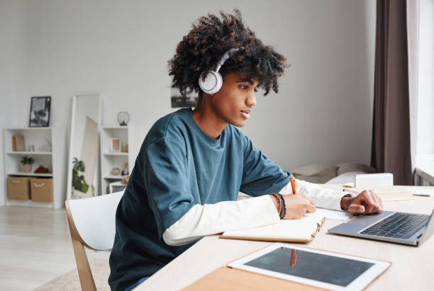 Teenager Doing Homework Side View Side view portrait of African-American teenage boy studying at home or in college dorm and using laptop, copy space homework stock pictures, royalty-free photos & images