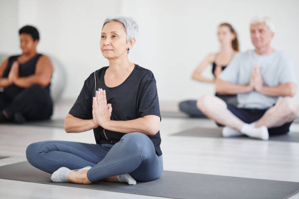 reife frau, die yoga im unterricht macht - floor women sitting yoga stock-fotos und bilder