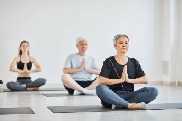 People relaxing during meditation Senior people sitting on mats in lotus position with eyes closed and meditating during yoga in class yoga studio photos stock pictures, royalty-free photos & images