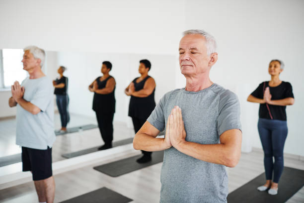 People meditating during training Group of senior people standing on mats with their eyes closed and meditating during training in gym yoga class stock pictures, royalty-free photos & images