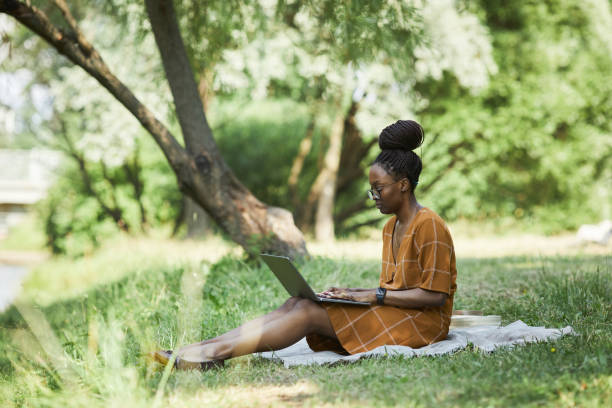 mulher afro-americana usando laptop no parque - laptop computer grass nature - fotografias e filmes do acervo