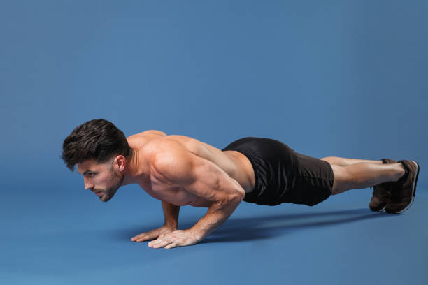 Full length portrait of young fitness sporty strong guy bare-chested muscular sportsman isolated on blue background. Workout sport motivation lifestyle concept. Doing push-ups exercises looking aside retrato de cuerpo entero de joven deportista de fitness y hombre fuerte con el pecho desnudo y musculoso aislado sobre fondo azul. concepto de estilo de vida de motivación deportiva de entrenamiento. hacer ejercicios de flexiones mirando a un lado.