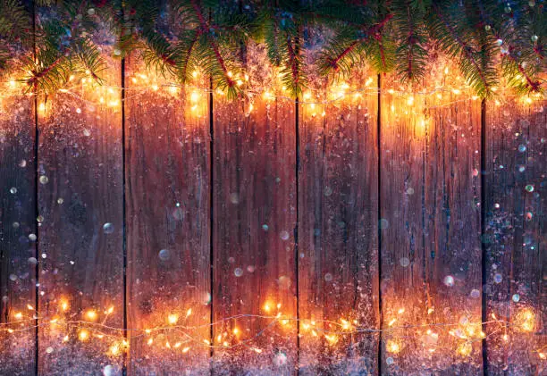 Christmas Lights - Decorations Illuminated With String Lights On Dark Wooden Board With Bokeh Snowflakes