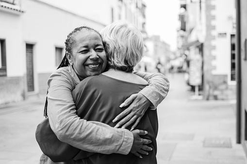 Multiracial senior women hugging each other - Elderly friendship and love concept - Focus on african woman face - Black and white edition
