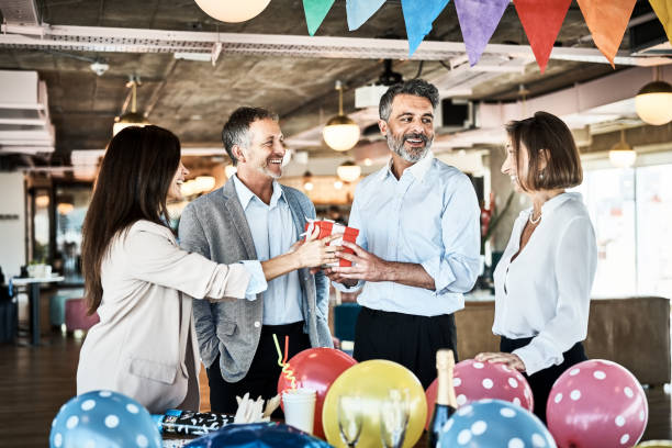 les gens d’affaires offrent un cadeau d’anniversaire à un collègue au bureau - men giving balloon women photos et images de collection