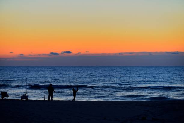 Unrecognizable adult man and his equal unrecognizable son fishing on the assateague island national seashore at dawn on a fine autumn day with the whole world before them