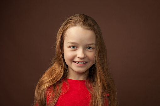 Close up studio portrait of 9 year old girl with long brown hair in red t-shirt on brown background