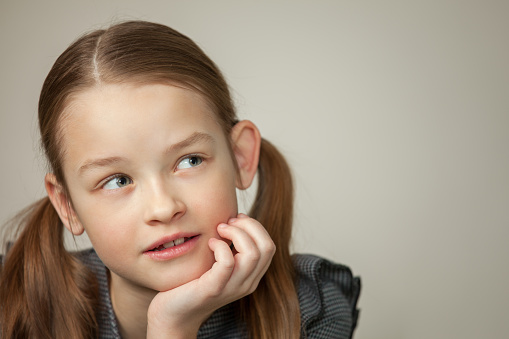 Close up studio portrait of 9 year old girl with long brown hair in gray dress on gray background