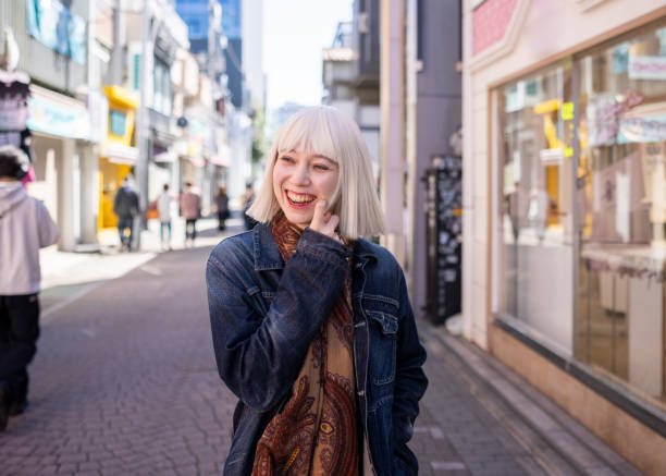 junge frau mit platinblonden haaren, die mit einem lächeln auf der einkaufsstraße spazieren geht - harajuku district stock-fotos und bilder