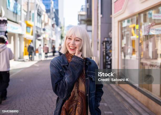 白いブロンドの髪の若い女性が笑顔で商店街を歩いている