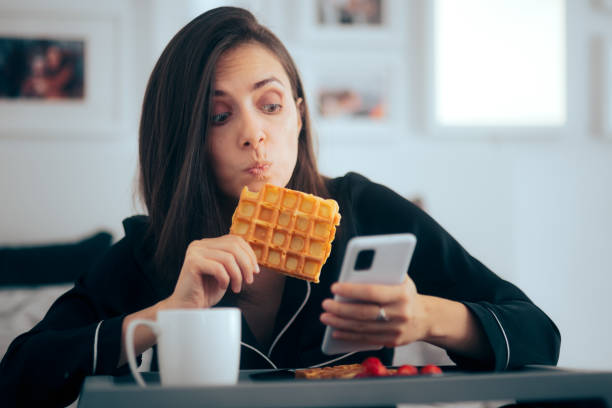 여자 먹는 와플 에 침대 확인 그녀의 스마트폰 - waffle eating meal food and drink 뉴스 사진 이미지