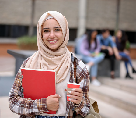 Portrait of a Happy female Muslim student smiling in college and holding a cup of coffee while looking at the camera - education concepts