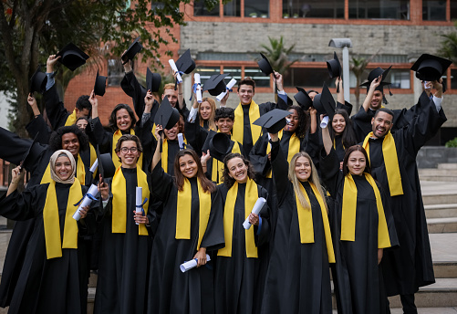 Happy group of students on their graduation ready to throw their mortar boards in the air and smiling - education concepts