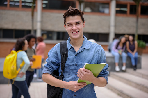 Portrait of a happy college student at the school holding his notebooks and looking at the camera smiling - education concepts