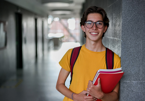 Portrait of a happy college student smiling in the hall while holding his notebooks and looking at the camera