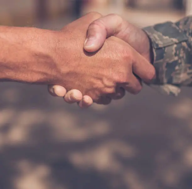 Soldier in Military Uniform Shaking Hands with Unidentified Male