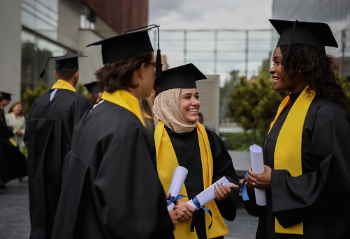 Multiracial group of graduate students talking outdoors after their graduation ceremony - education concepts