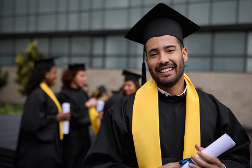 A female University student of Middle Eastern decent smiles proudly on graduation day.  She is dressed formally in a gown and cap.