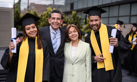 Portrait of happy Latin American graduate students smiling with their parents on their graduation day while looking at the camera - education concepts