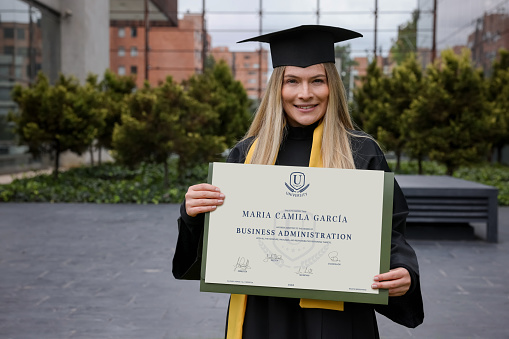 Portrait of a happy graduate student holding her business diploma and looking at the camera smiling - graduation day concepts **DESIGN OF DIPLOMA BELONGS TO US**