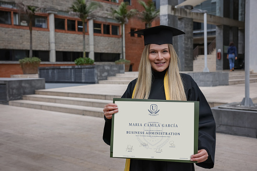 Portrait of a happy graduate student holding her diploma in business administration and looking at the camera smiling - education concepts. **DESIGN OF DIPLOMA BELONGS TO US**