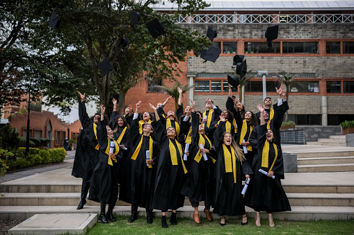 Group of graduates throwing their mortarboards in the air on their graduation day while holding their diplomas - education