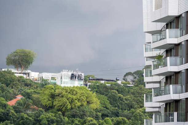 Modern residential area at Mt Faber in Singapore. People live in small compact smart home apartments close to the neighbour and surrounded by green tropical rainforest. Cable cars take people to their homes on the mountain. Seen just before the thunder hits the area.