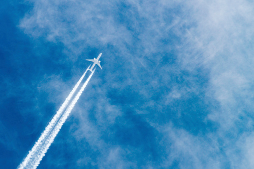 Airplane flying with high speed on blue sky background seen from the ground.